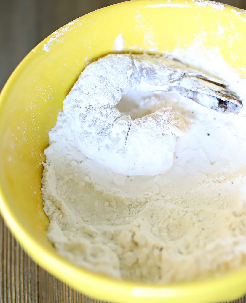 One shrimp being dipped and coated in a bowl with flour.