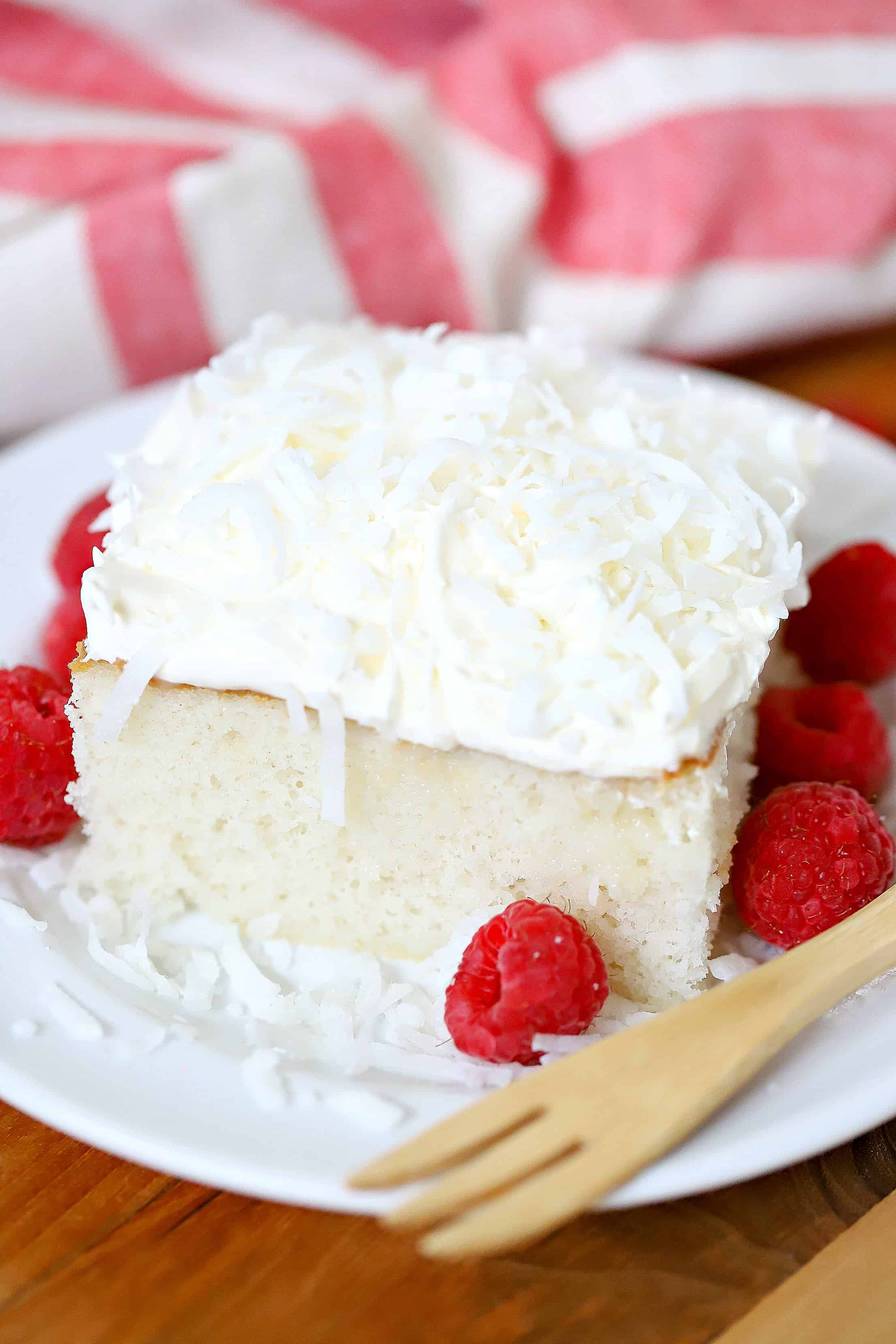 Piece of cake on a white plate with a side of raspberries and a fork.