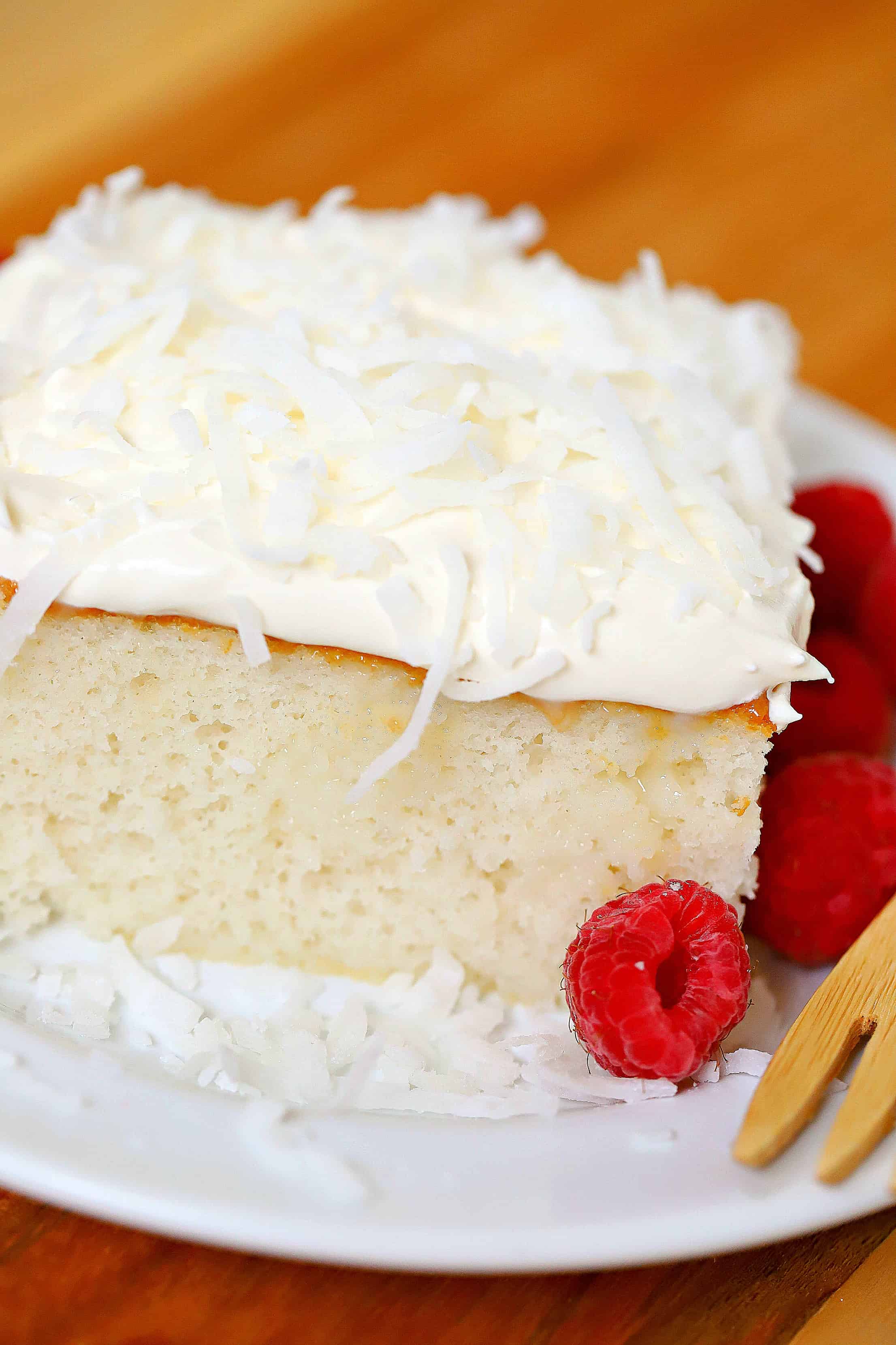 Coconut Cream Cake topped with whipped cream and coconut and a side of raspberries.