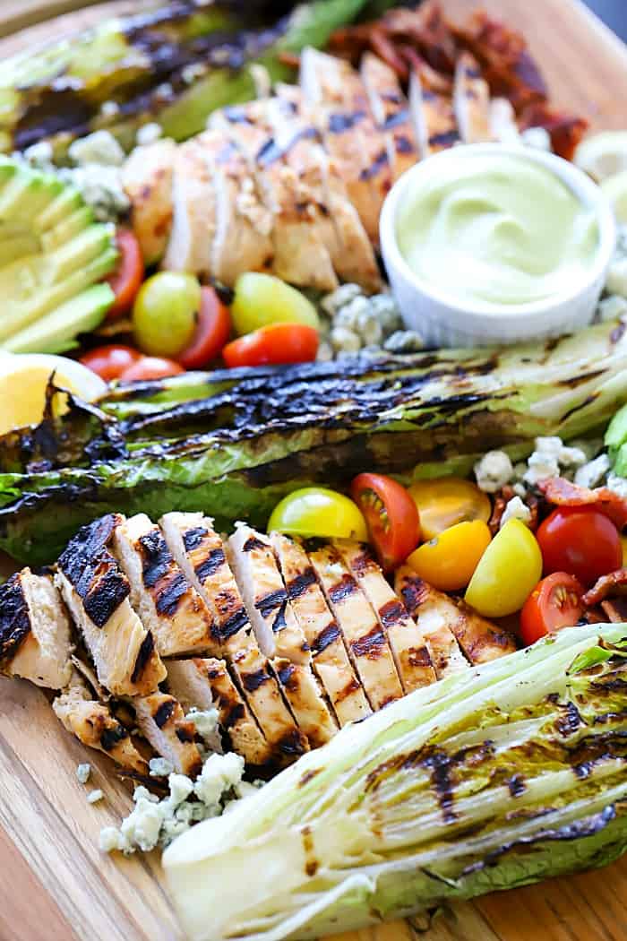 Delicious view of a platter of Cobb salad ingredients: marinated and grilled chicken, grilled romaine, cherry tomatoes, avocado, blue cheese and bacon.