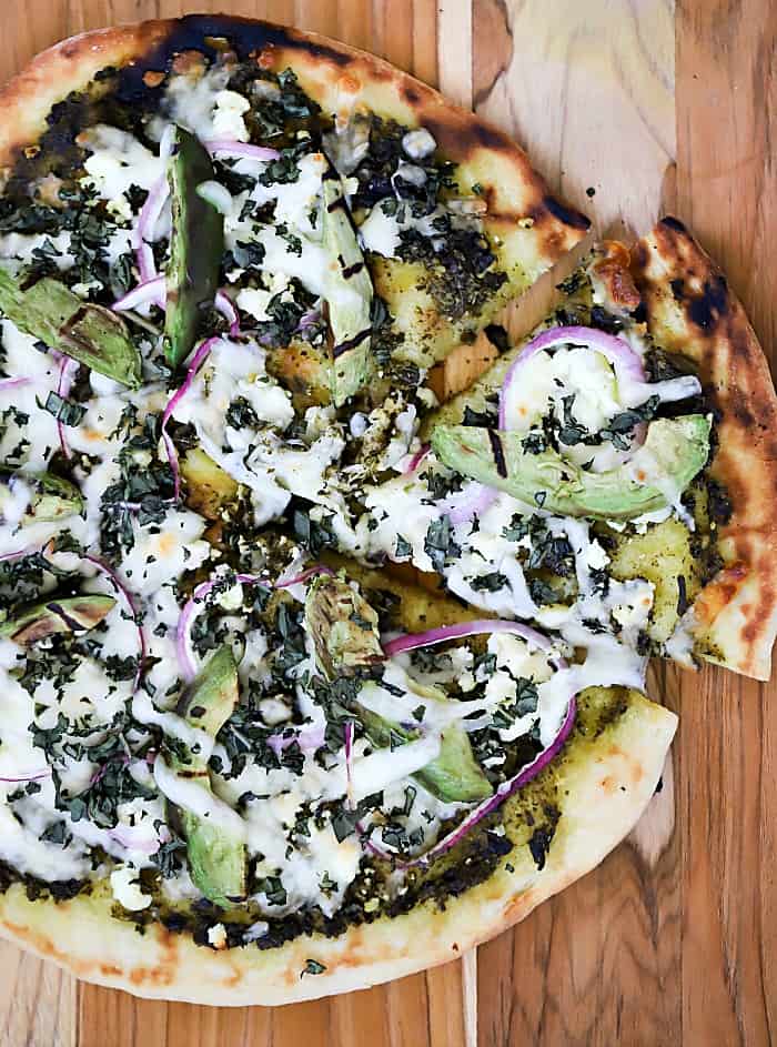 Overhead view of finished grilled pesto pizza with a slice pulled slightly out.
