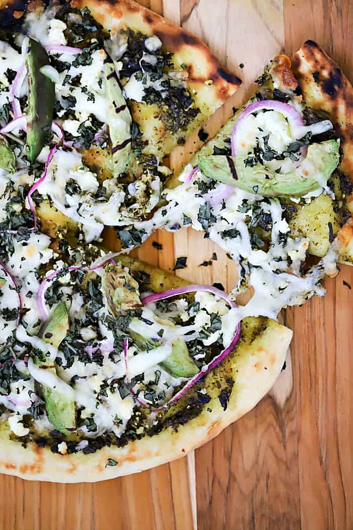 Overhead close up view of finished grilled pizza with a slice pulled slightly out.