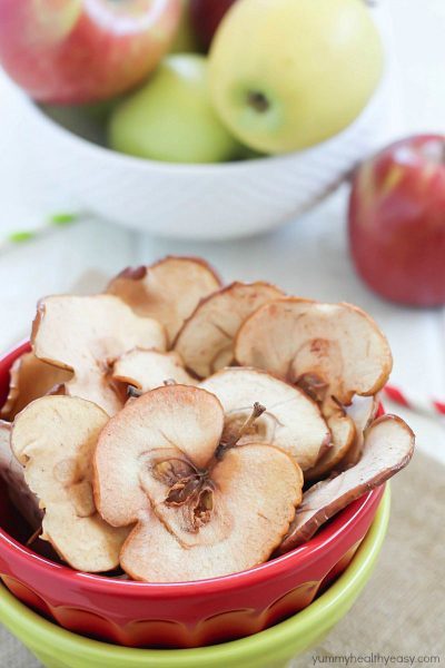 Homemade Apple Chips in a red and green bowl with fresh apples in the background.