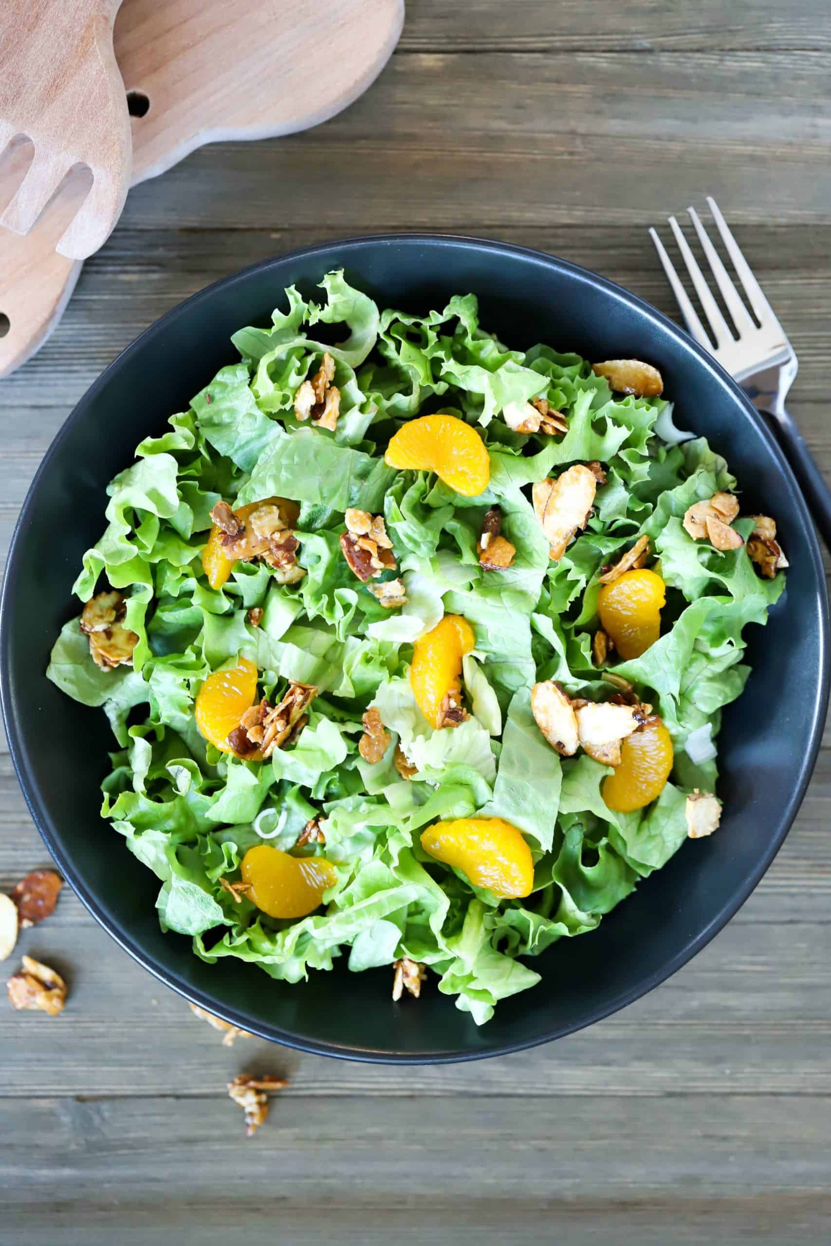 Overhead view of a black plate filled with lettuce, mandarin oranges and toasted almonds.