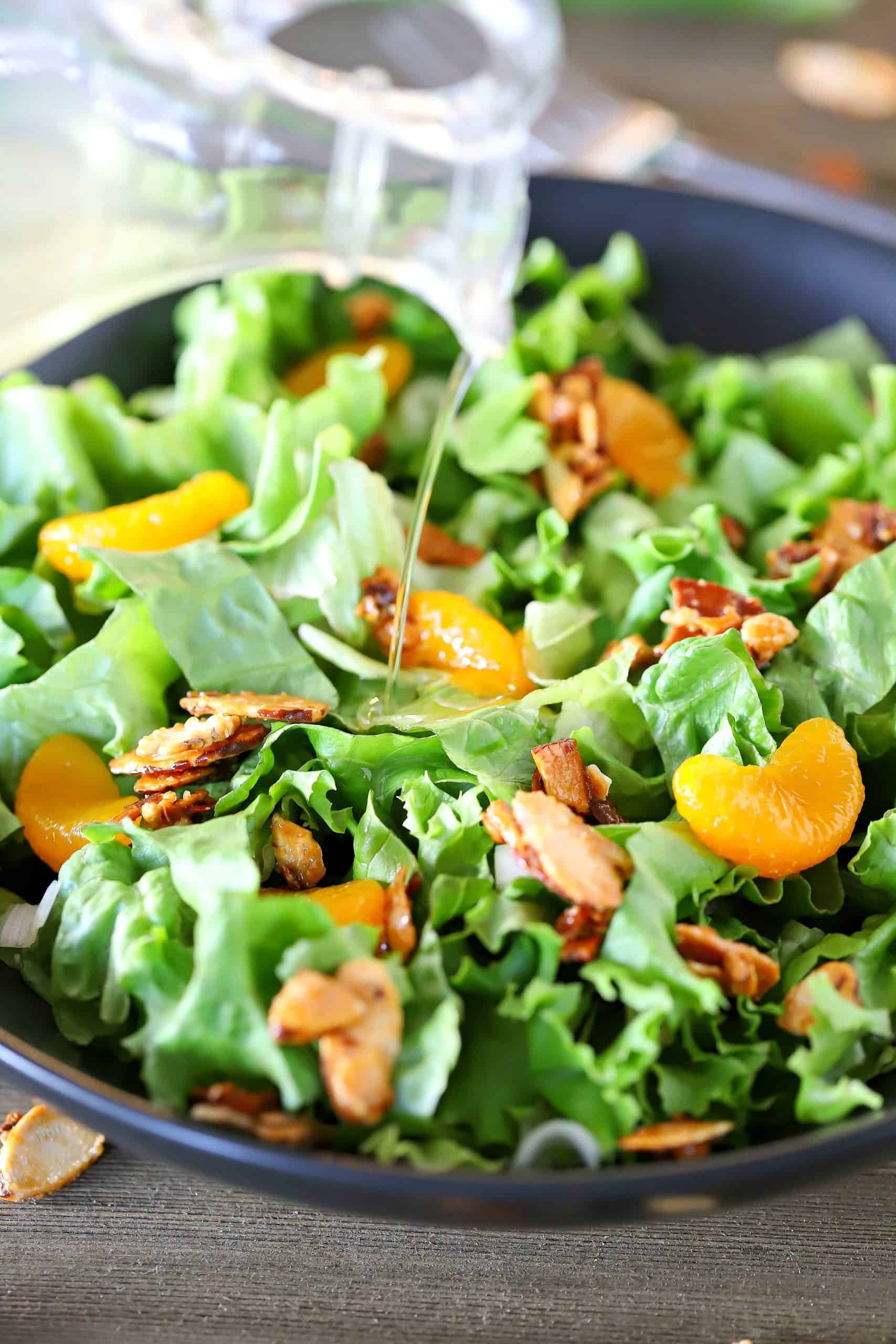 Dressing being poured over a bowl of lettuce, mandarin oranges and toasted almonds.
