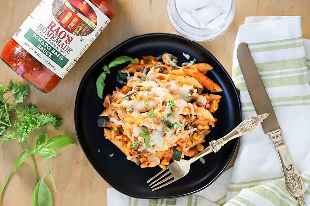 Top view of pasta plate with herbs and silverware and a glass of water next to it.
