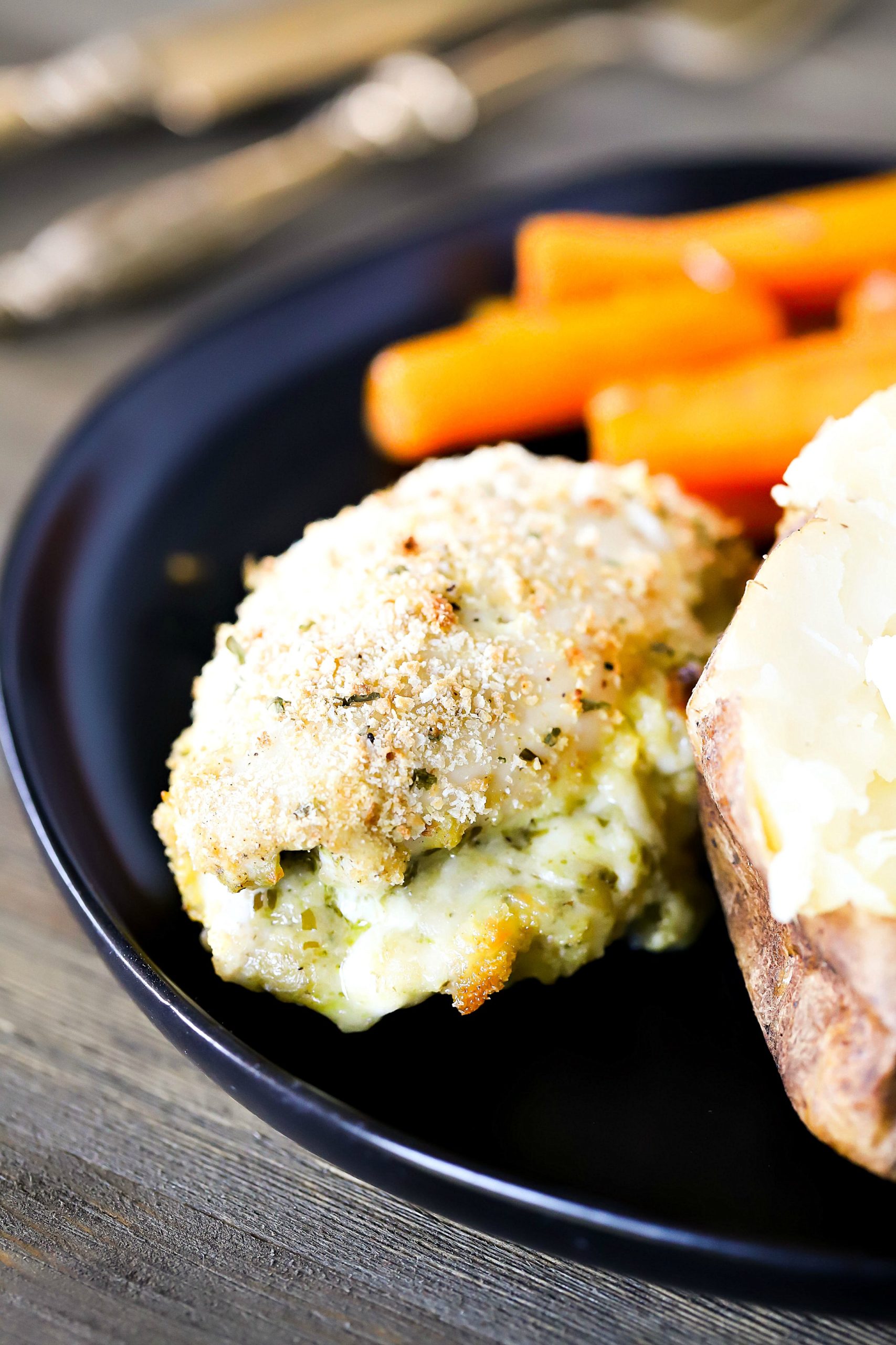 Chicken on a black plate with a side of carrots and baked potato