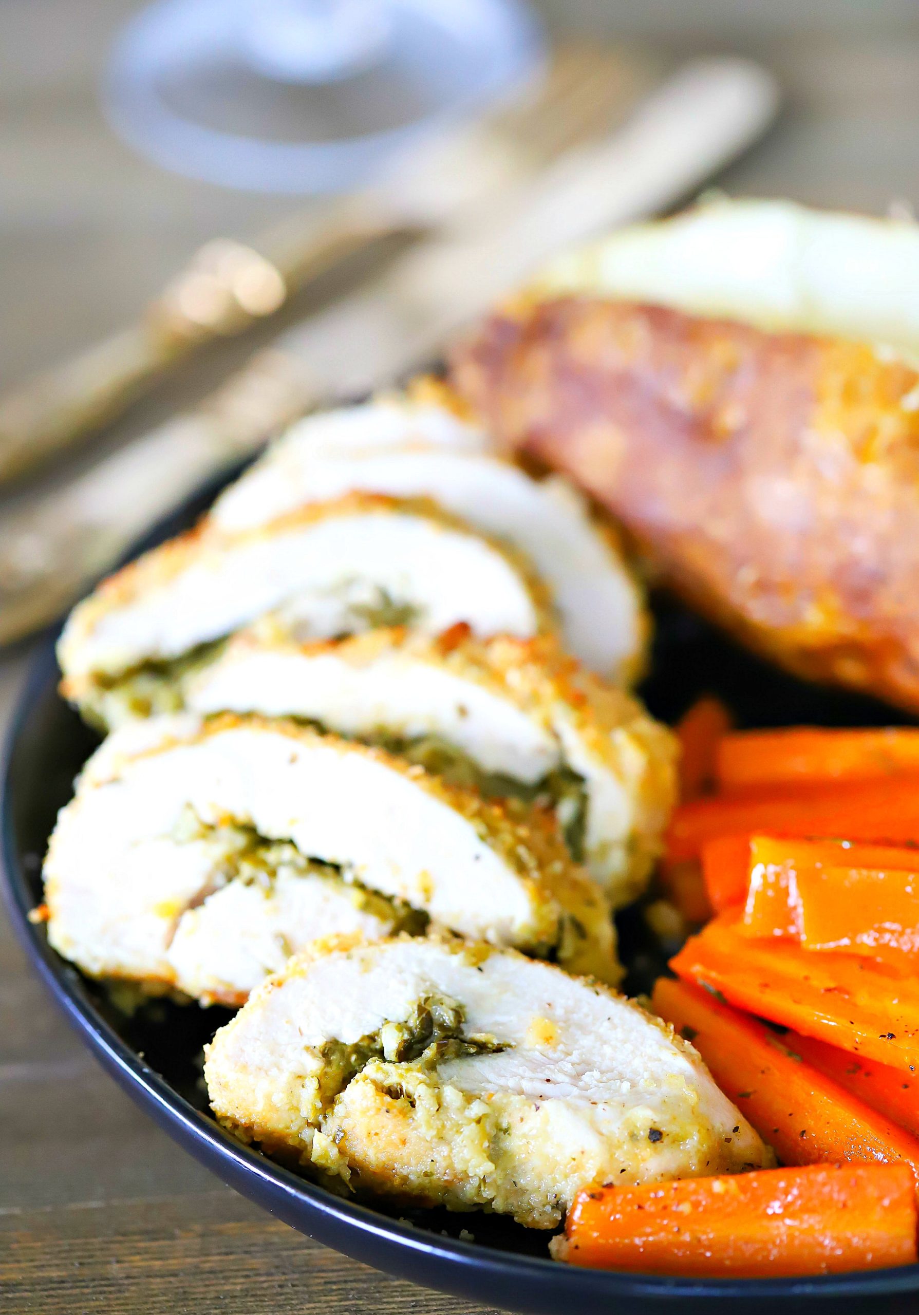 Sliced Pesto Stuffed Chicken on a black plate with a side of carrots