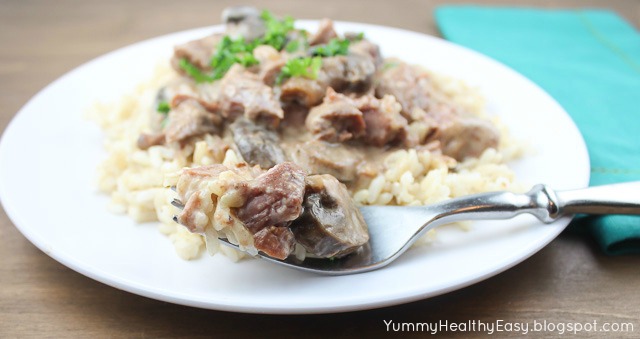 White plate with brown rice topped with beef stroganoff and fork in the front of the plate.